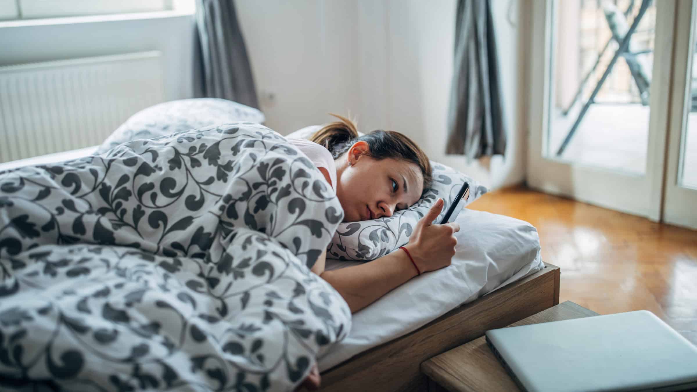Overcome Fatigue: 7 Causes & Solutions to Restore Energy 5 tired in bed looking at phone 1203519740
